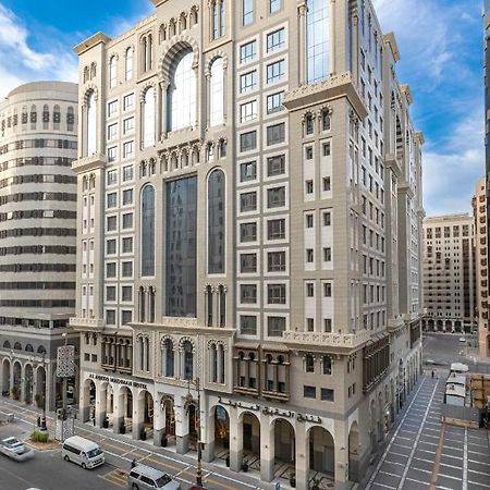 Al Aqeeq Madinah Hotel Medina Eksteriør billede The photo depicts a large, modern building with a distinctive architectural style. The structure shows a blend of classic and contemporary design elements, featuring ornate details, large glass windows, and a prominent central facade. Surrounding the