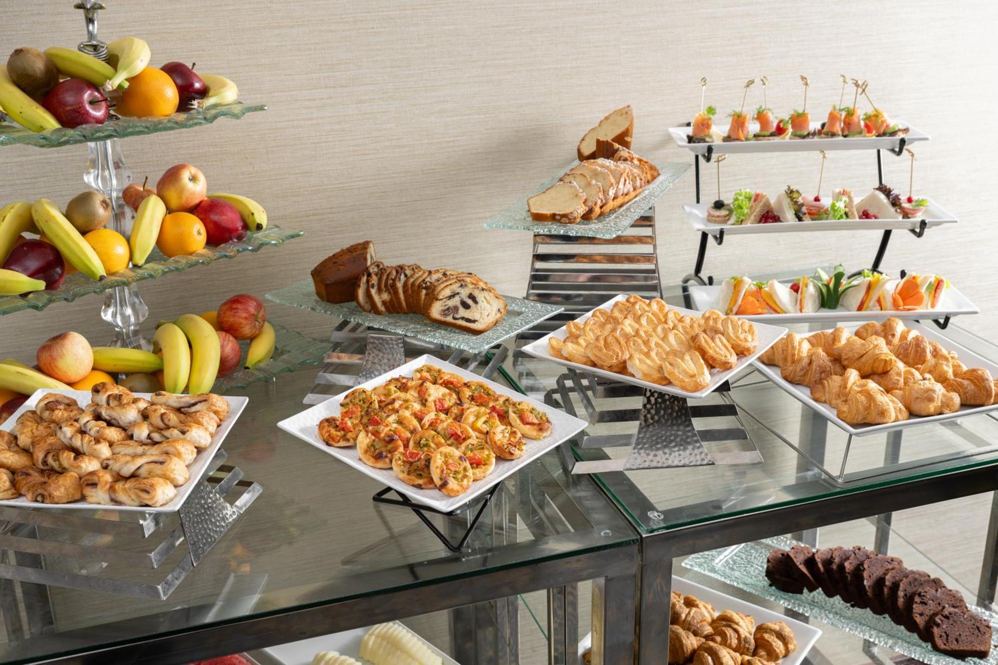 Al Aqeeq Madinah Hotel Medina Eksteriør billede The photo showcases a buffet-style spread featuring a variety of food items. There are several platters with appetizers, including seafood dishes, pastries, and other savory items. In addition, there is a selection of fresh fruit displayed on a glass