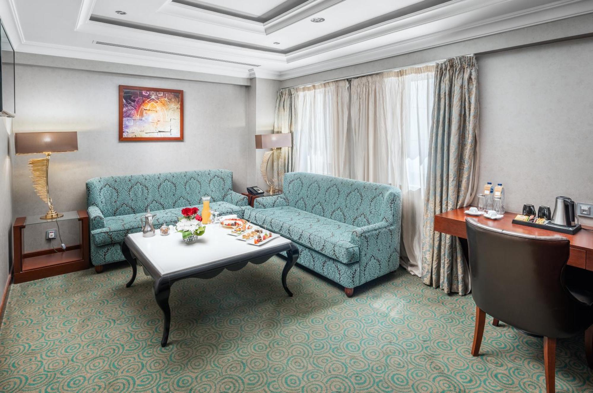 Al Aqeeq Madinah Hotel Medina Eksteriør billede The photo shows a cozy hotel room or lounge area. It features two light blue sofas arranged around a low coffee table. On the table, there are snacks or refreshments arranged aesthetically. The room has a neutral color palette with a textured carpet 