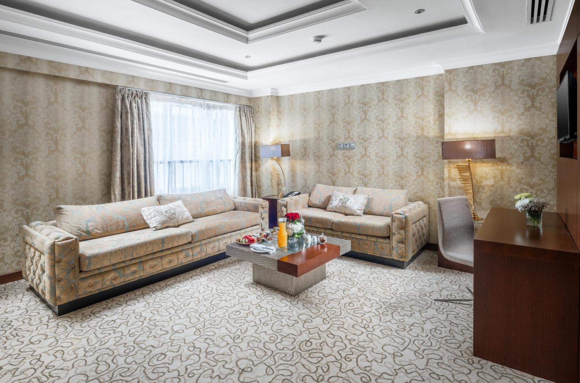 Al Aqeeq Madinah Hotel Medina Eksteriør billede The photo shows a stylish living room with an elegant design. There are two beige sofas placed opposite each other, adorned with decorative pillows. A low coffee table is positioned in the center, featuring various items, possibly drinks or decorativ