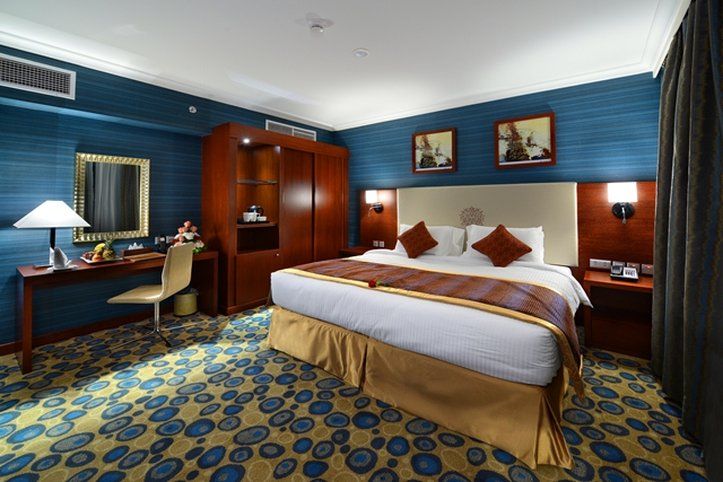 Al Aqeeq Madinah Hotel Medina Eksteriør billede The photo shows a hotel room designed with a modern and stylish aesthetic. It features a large bed with a cream-colored headboard and decorative pillows. The room is decorated with blue walls and patterned carpet, creating a cozy atmosphere. 

There 